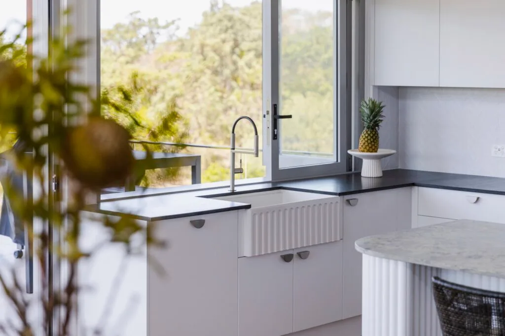 A minimalist kitchen with a white sink and black benchtop.