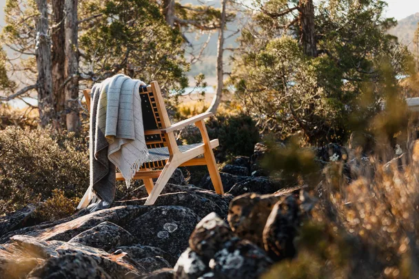 A timber chair and throw rug in a bush landscape.