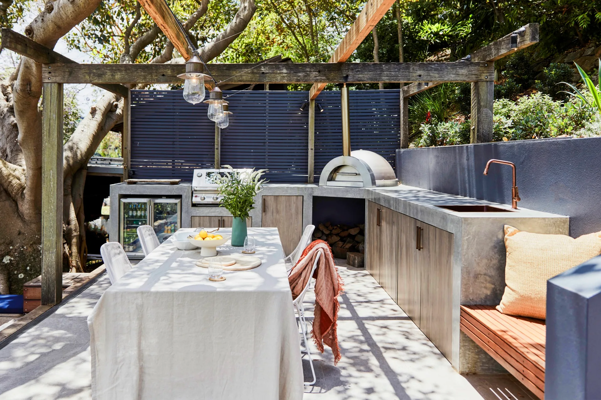 An outdoor kitchen with a concrete bench, pizza oven and hanging festoon lights.