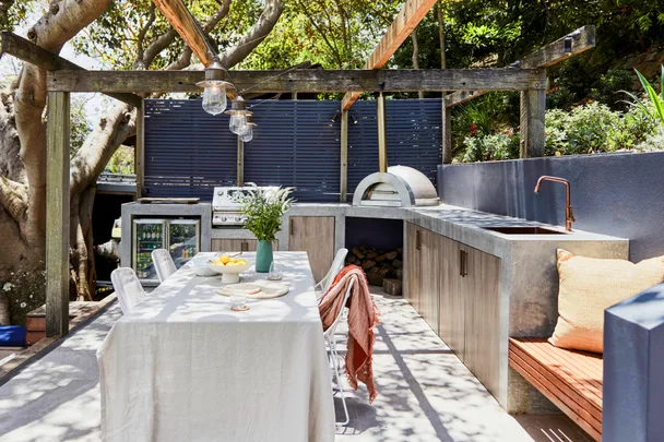 An outdoor kitchen with a concrete bench, pizza oven and hanging festoon lights.