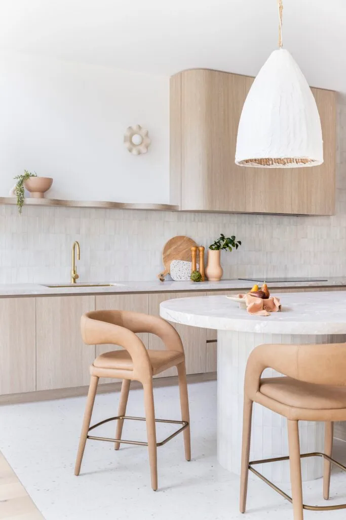 A curved island with tan stools by timber cabinets and functional cooking area.