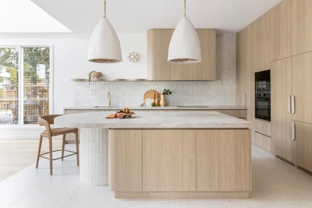 A minimalist kitchen with timber-style joinery, a curved island and neutral subway tiles.