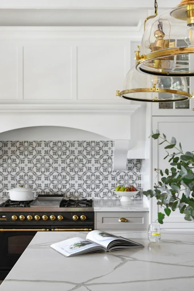 A country style kitchen with a marble island, vintage style lights and a mosaic splashback.