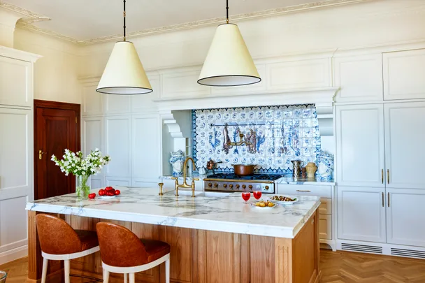 A Spanish-style kitchen with a blue-tiled splashback, marble island and shaker cabinets.