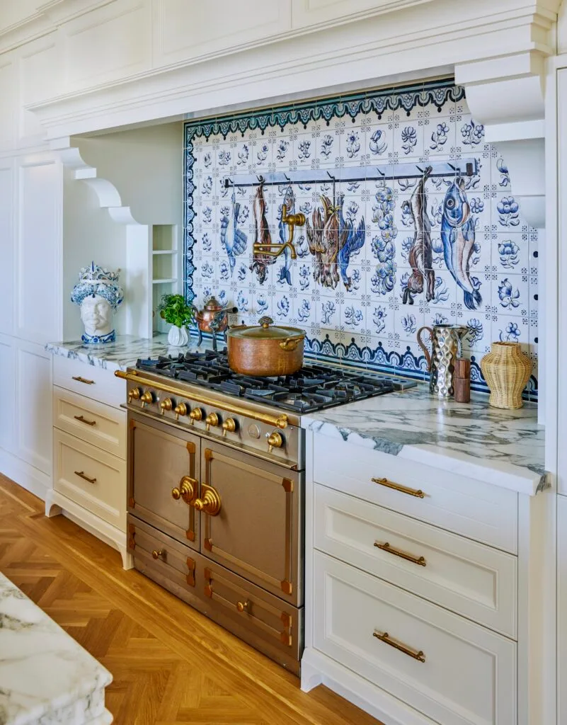 A classic brass cooker and stove beneath a Spanish splashback mural.