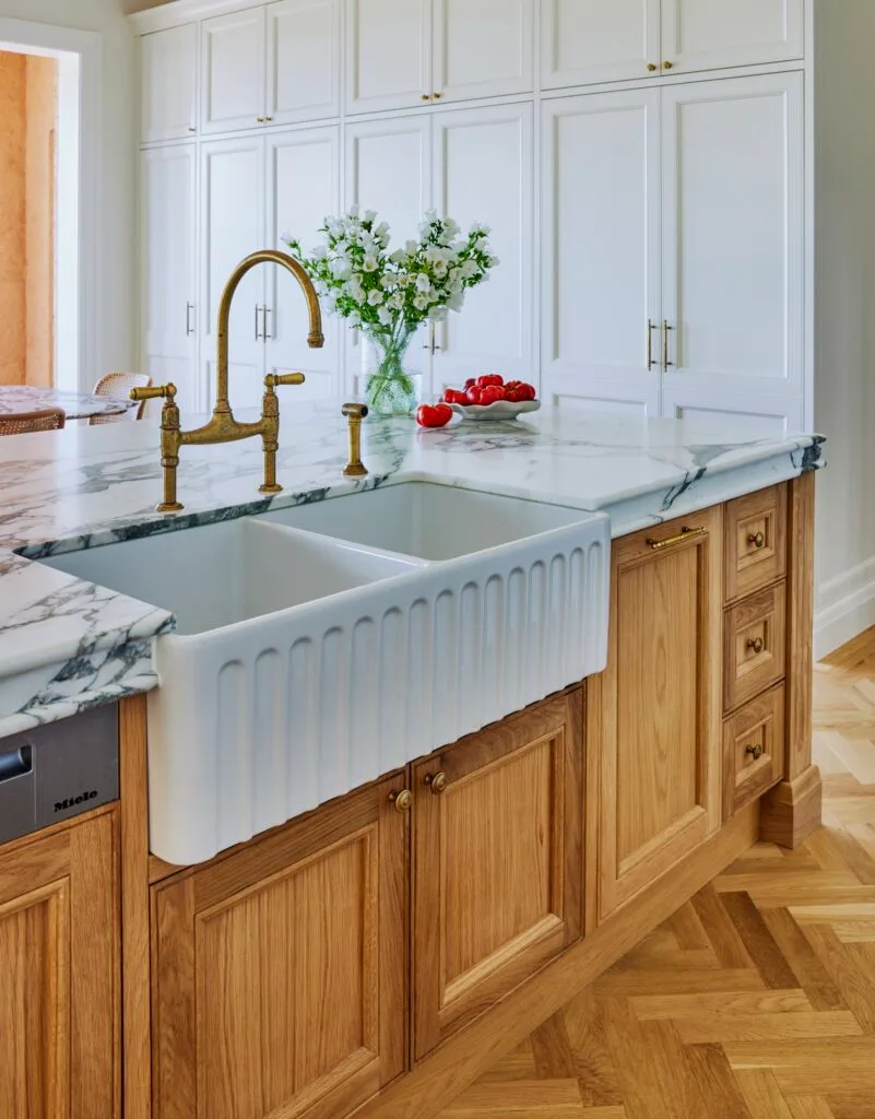 A farmhouse sink inset in a marble island with brass-style tapware.