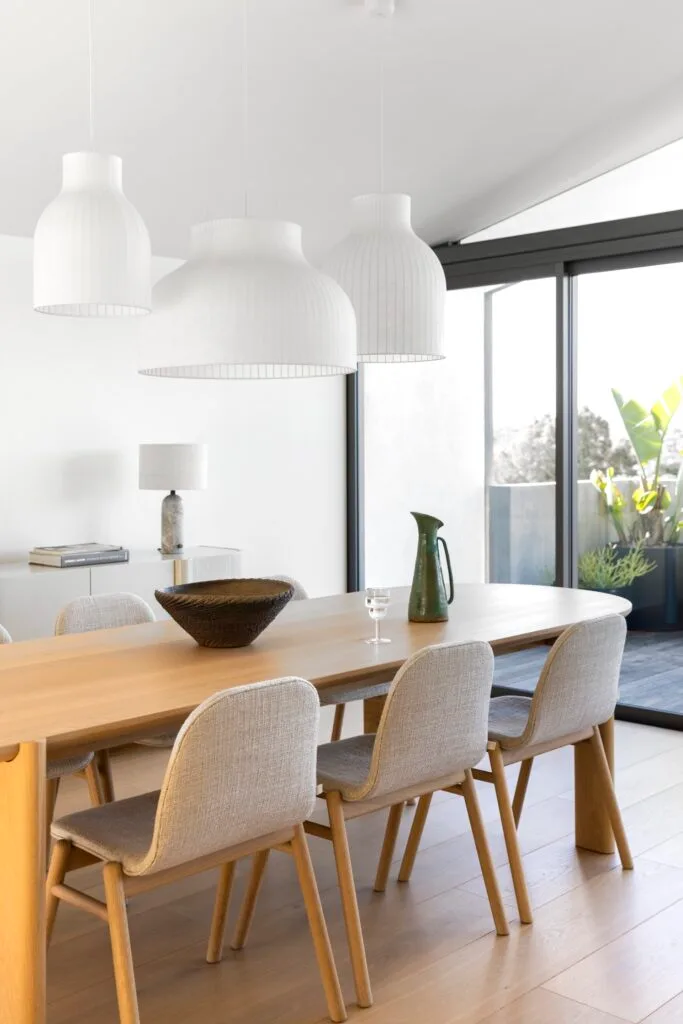 A timber dining room table and rounded white pendants above.