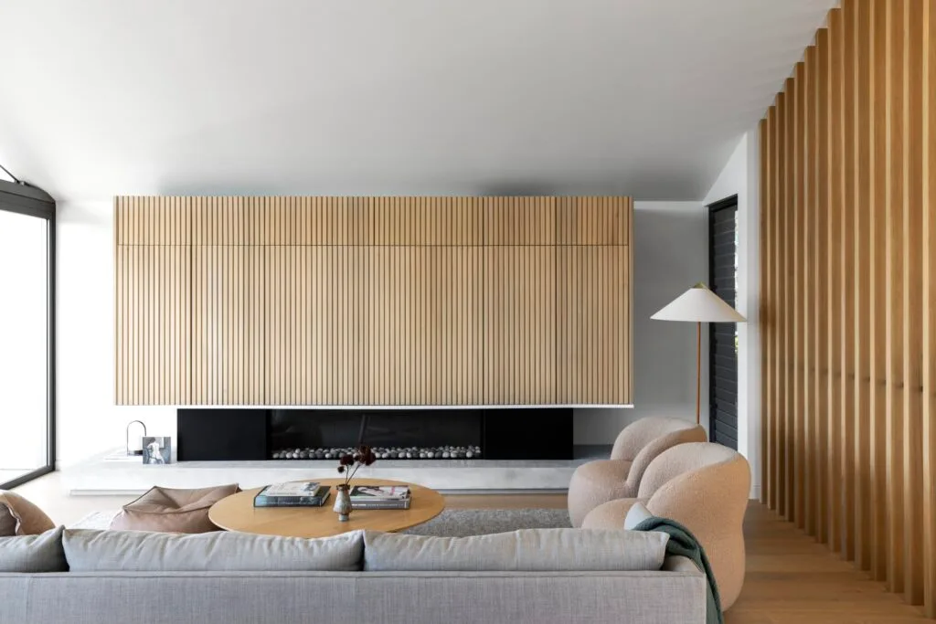 A Scandinavian style living room with fluted timber walls, a fireplace and curved chairs.