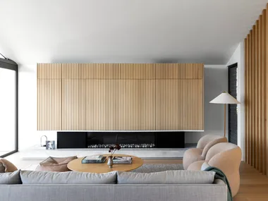 A Scandinavian style living room with fluted timber walls, a fireplace and curved chairs.
