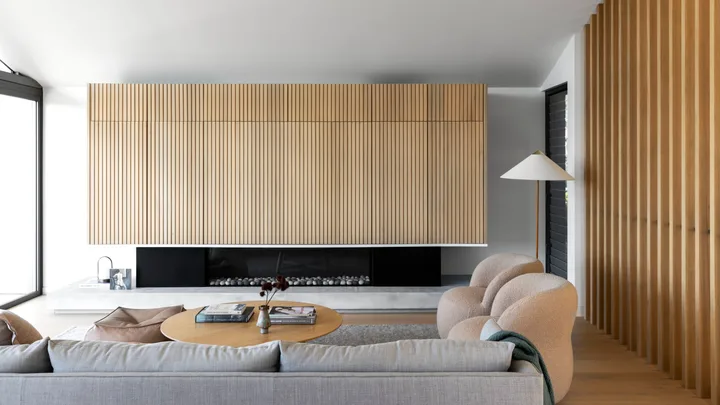 A Scandinavian style living room with fluted timber walls, a fireplace and curved chairs.