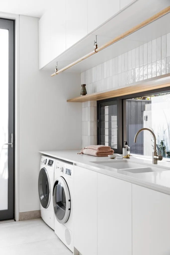 A laundry with white subway tiles, cabinets and a benchtop.