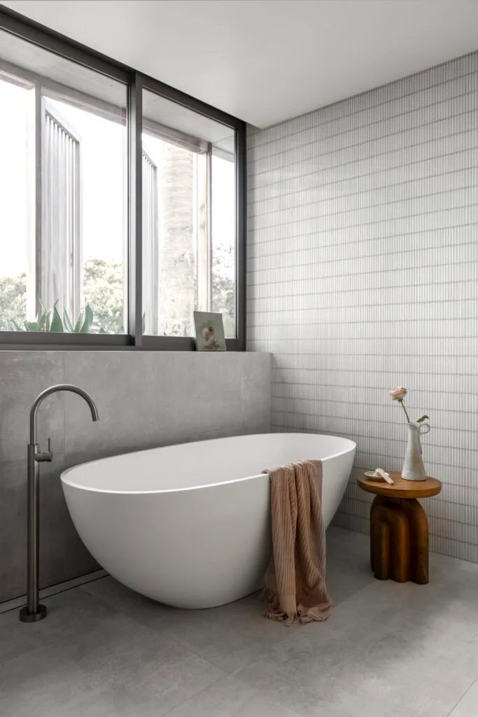 A modern ensuite with a freestanding bath and neutral walls with finger tiles.