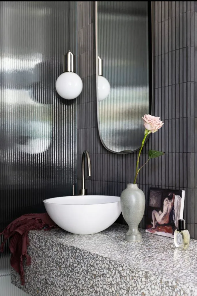 A powder room with dark finger tiles, stone vanity and fluted glass door.