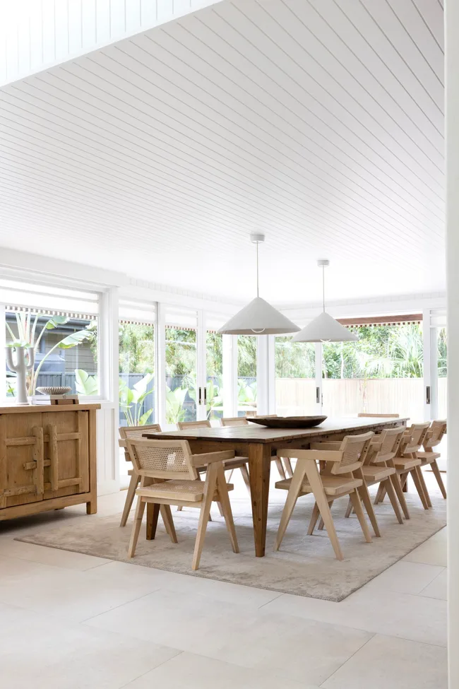 A dining area with a panelled white ceiling, timber table and hanging pendants.