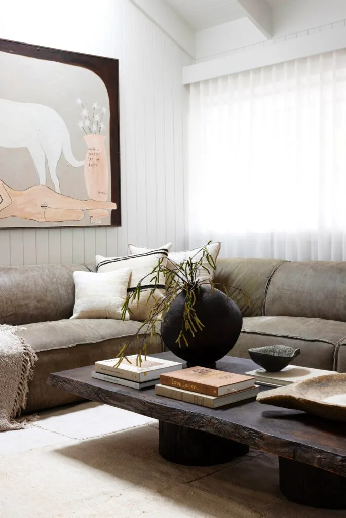 A living room with white panelled walls, a rustic timber coffee table and brown leather style sofa.