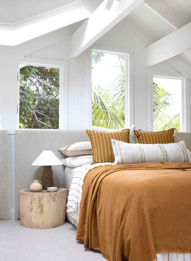 A coastal bedroom with vaulted ceilings and a bed with orange linen.