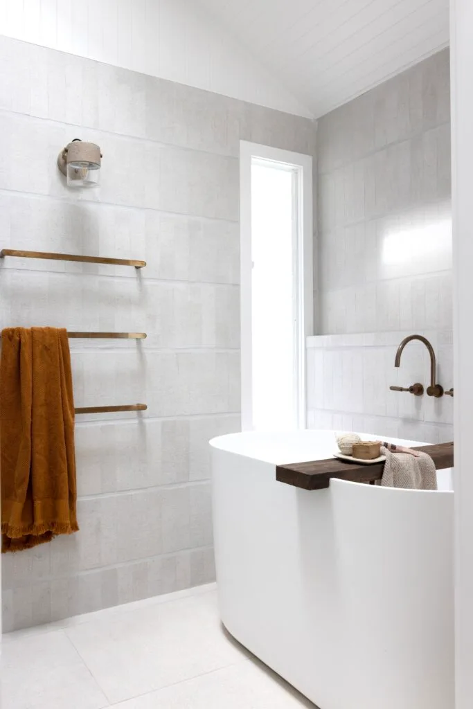 A neutral bathroom with a freestanding bath and brass style railings.