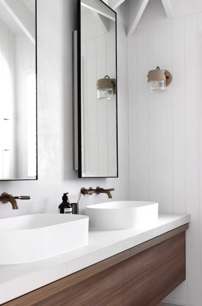 A white bathroom with a double timber vanity and panelled wall detailing.