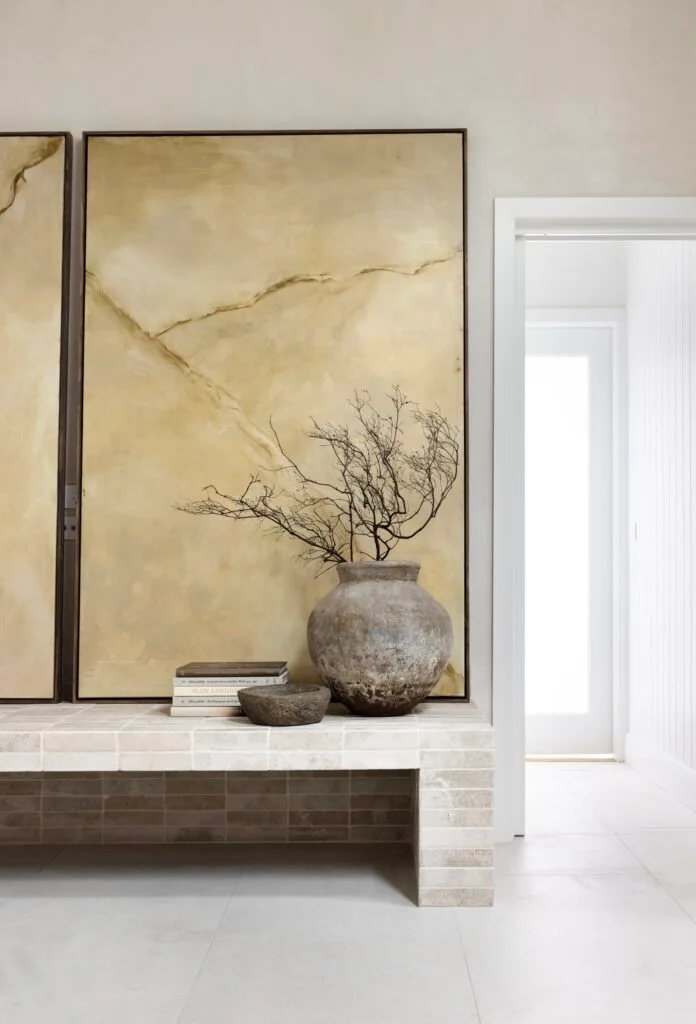 A pair of minimalist, neutral artworks on a bench by a stone vessel.