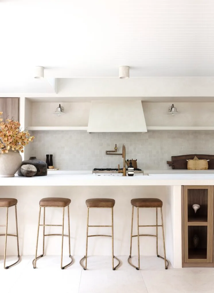 A neutral coastal kitchen with an island, brass tapware and angled range hood by the stove.