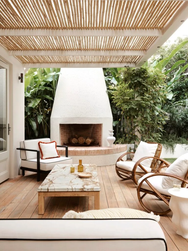 A tropical outdoor entertaining area with rattan chairs and a carved fireplace.