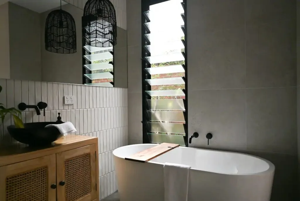 A modern bathroom with grey tiling, a freestanding bath and timber details.