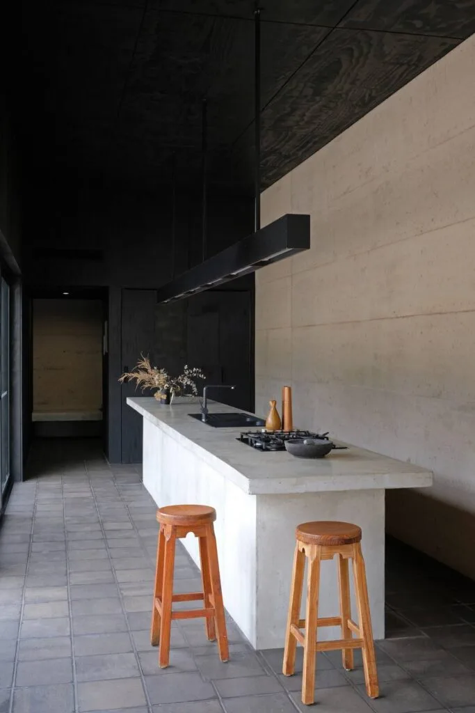 A modernist kitchen with a long, white marble island and black timber ceiling.