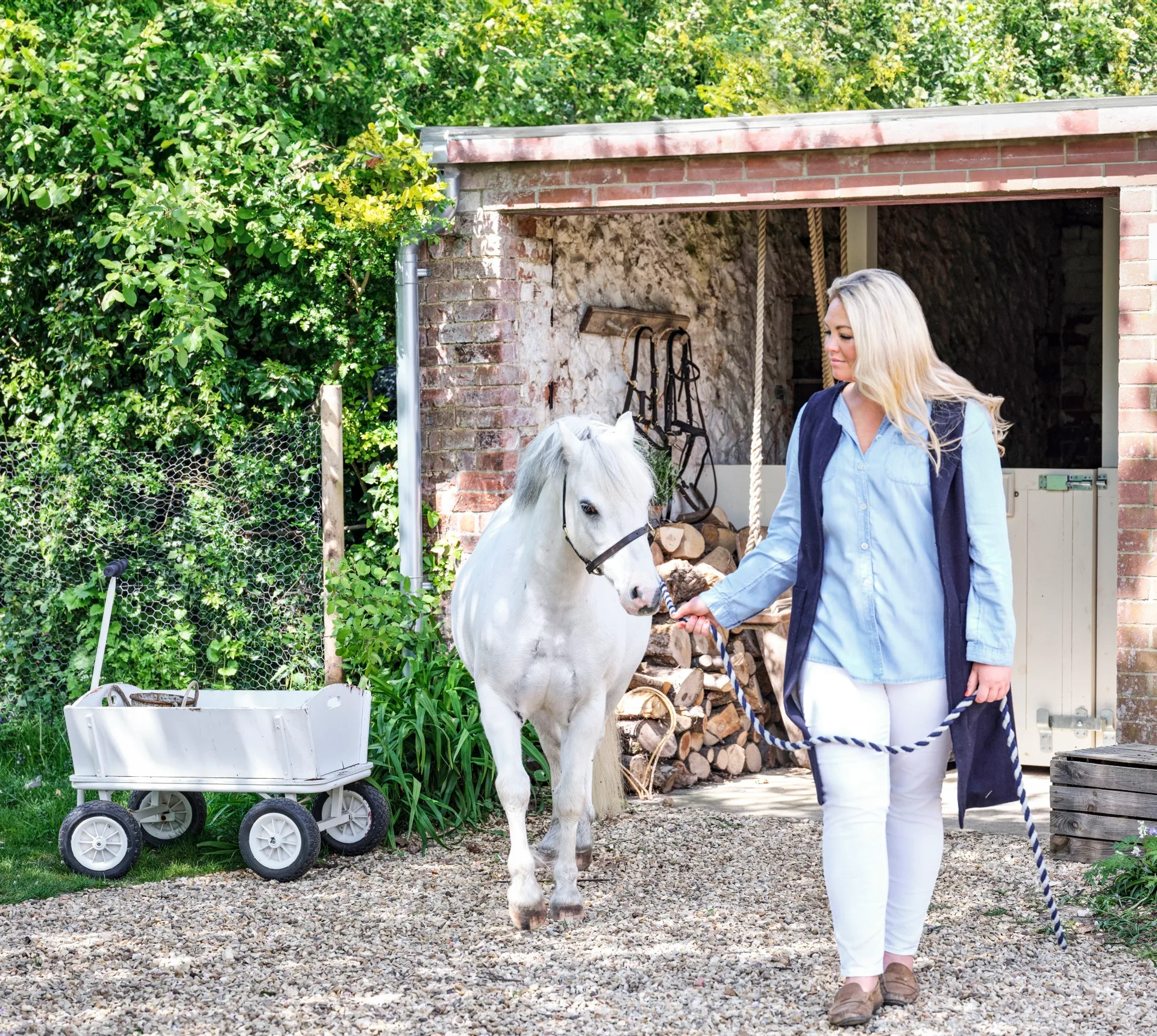 Owner Sophie leading a white pony near the stables.