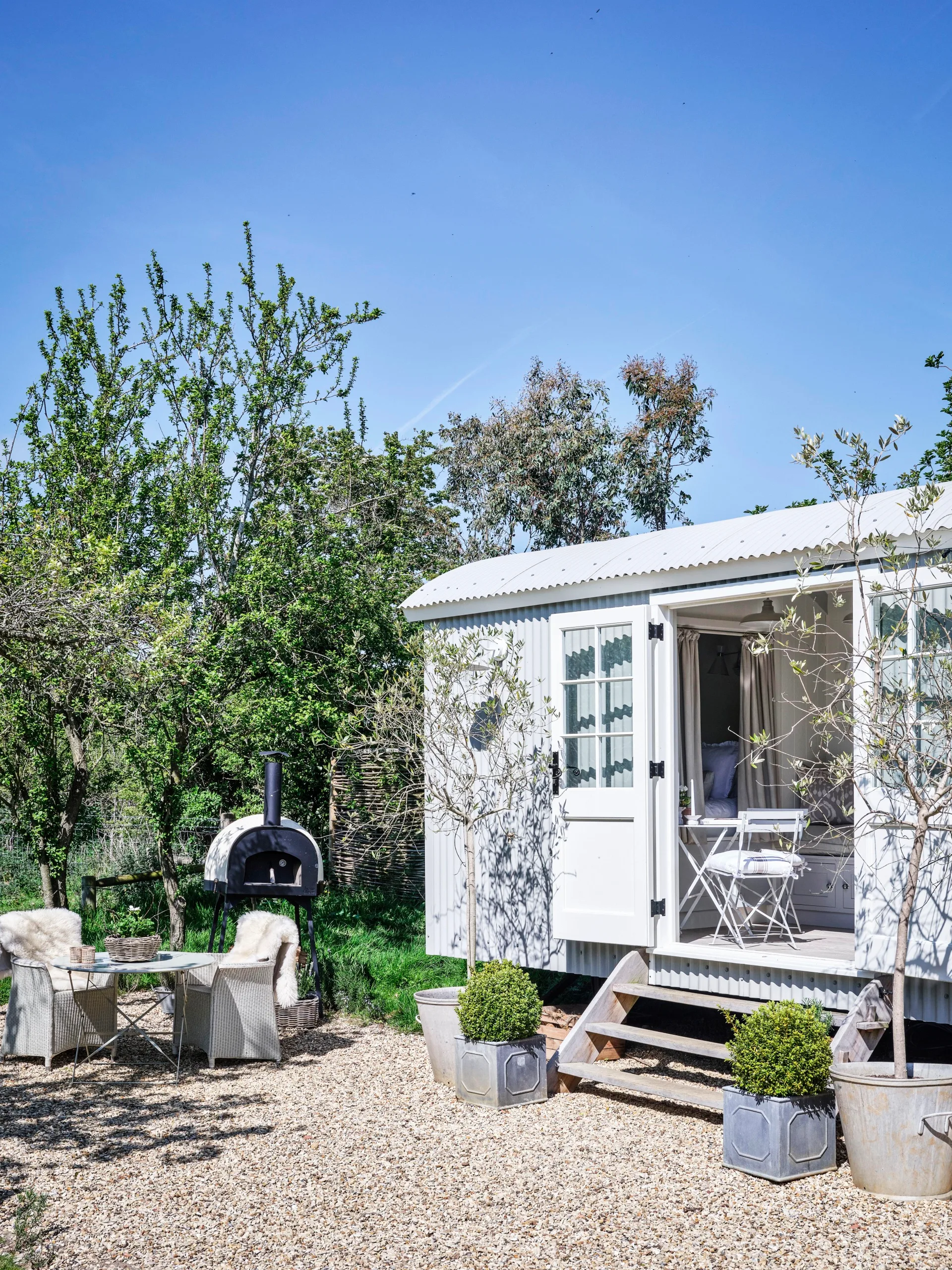 The shepherd hut exterior with an outdoor seating area and pizza oven.