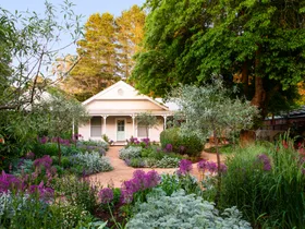 A blooming garden with a meandering path to a weatherboard cottage.