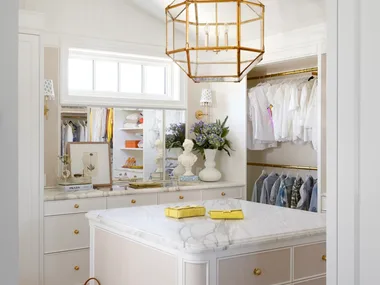 A white dressing room with a gold geometric pendant and marble drawers.