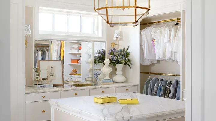 A white dressing room with a gold geometric pendant and marble drawers.