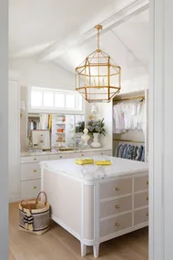 A white dressing room with a gold geometric pendant and marble drawers.