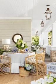 An outdoor alfresco area with cane chairs, a tablescape with flowers and hanging pendants.