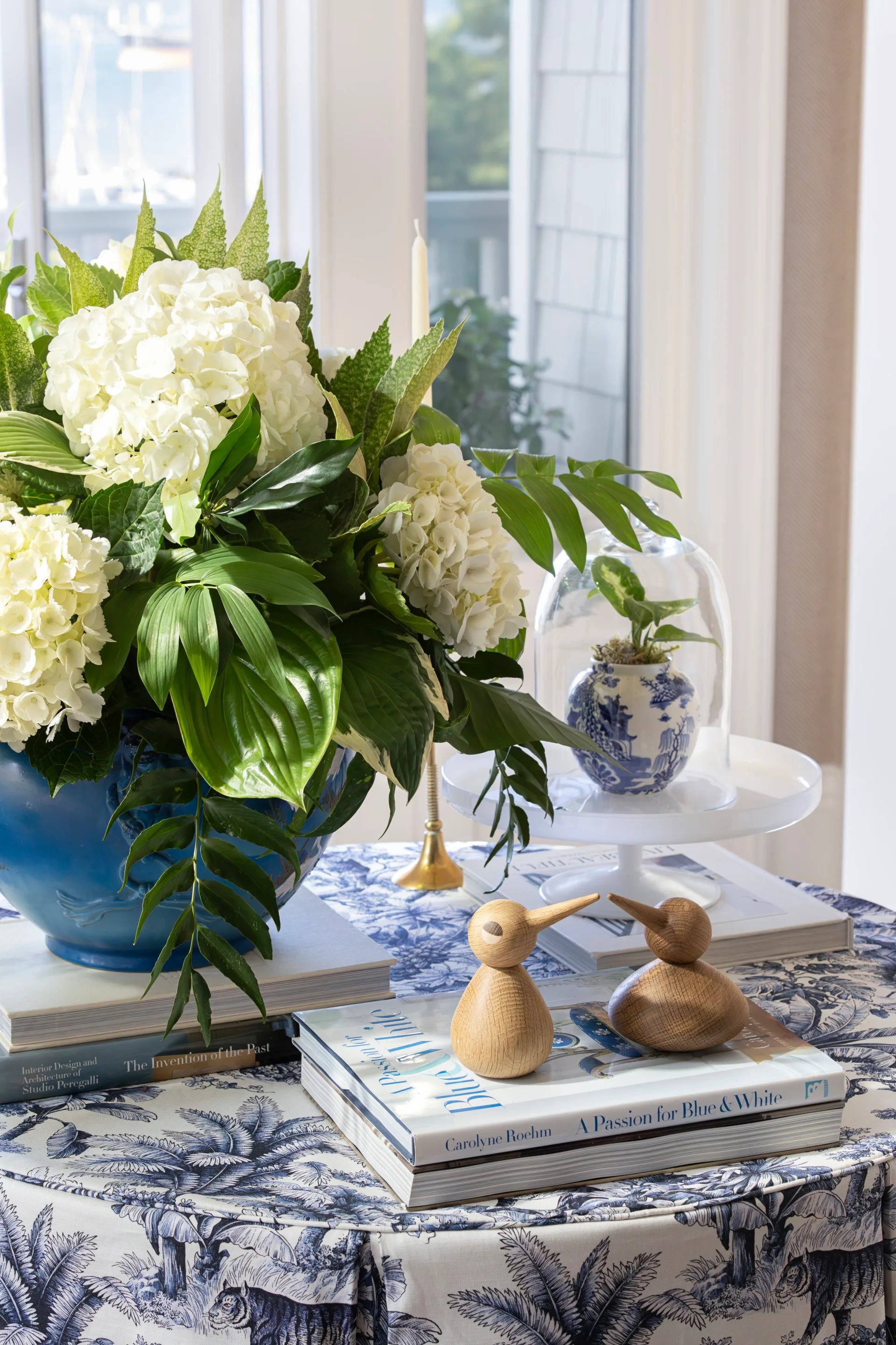 A table decorated with a vase of white flowers, books and wooden birds.