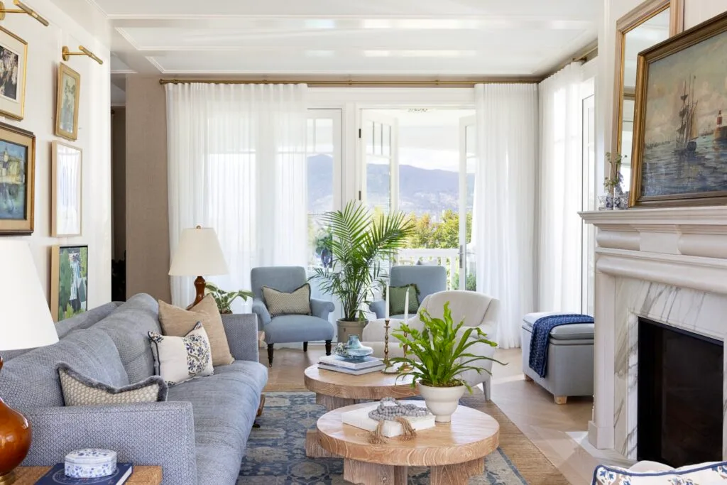 A coastal style living area with blue sofas, a marble fireplace and nautical wall art.