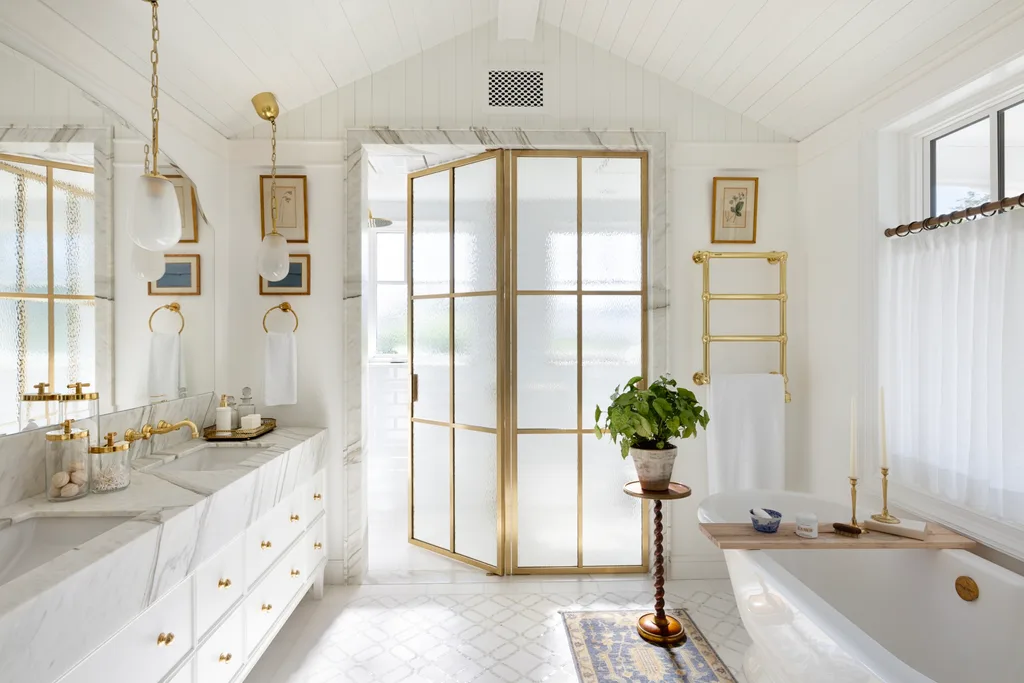 An all-white ensuite with gold glass doors, a freestanding bath and a marble vanity.