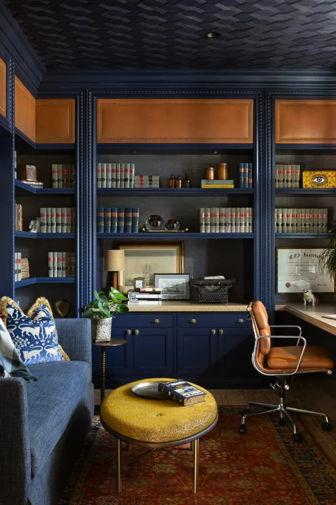 A home office with a navy library and walls, sofa and desk.