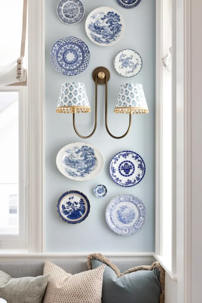 A wall gallery with decorative blue plates and two sconces.