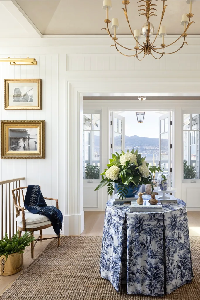 A white upper landing decorated with a jute rug, gold chandelier and a table with a patterned cover.