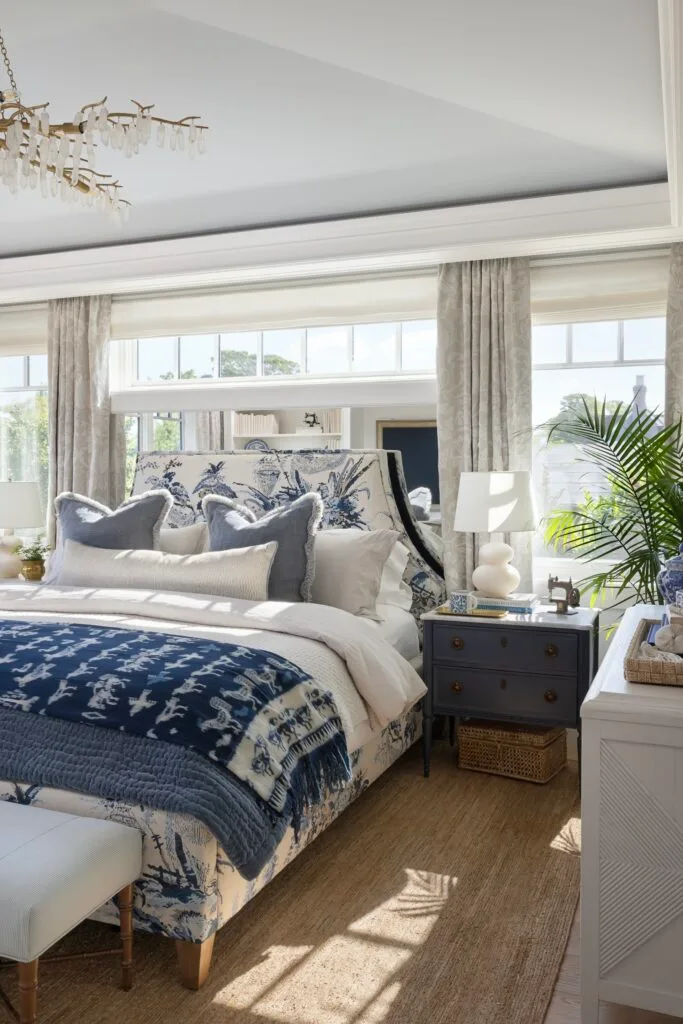 A coastal style main bedroom with blue furnishings, a gold chandelier and a jute rug.