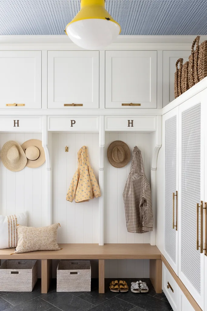 A classic mudroom with a timber bench, white wall panels and cupboards.