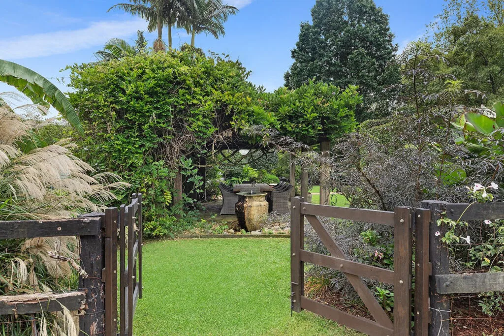 Gate leading to lush grassy entertaining area and outdoor dining setting shaded by a wisteria arbour.