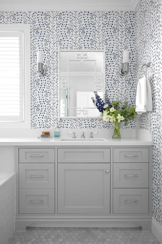 A classic bathroom with a shaker style vanity and blue wallpaper.