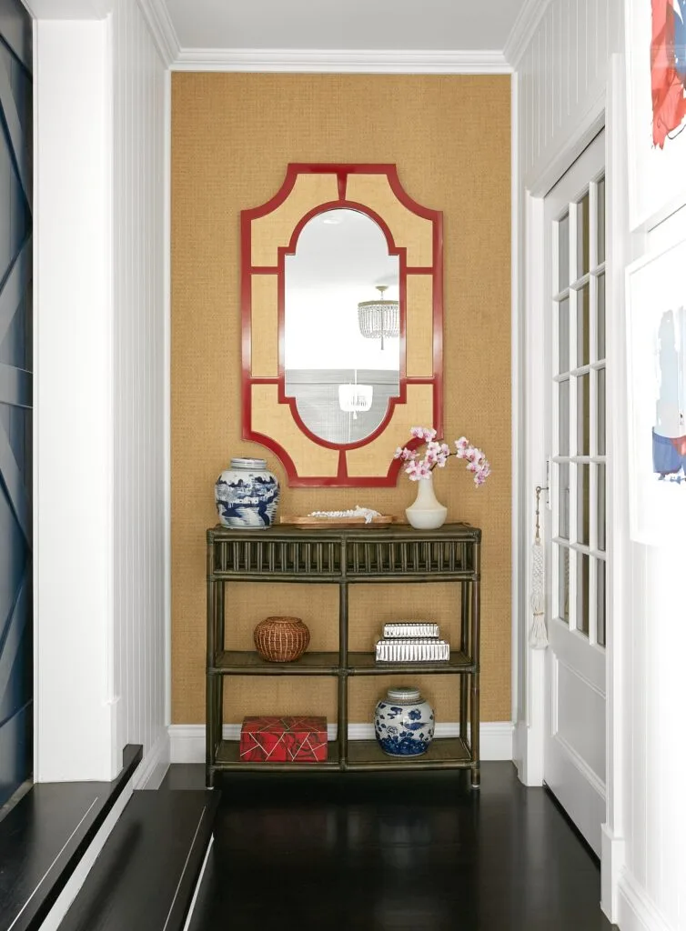 A foyer with a custom red and white mirror and cane console.