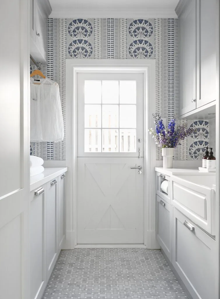 A laundry room with blue patterned wallpaper and a farm-style door.