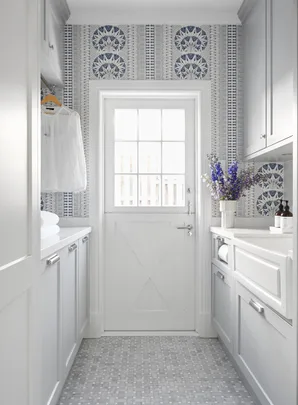 A laundry room with blue patterned wallpaper and a farm-style door.