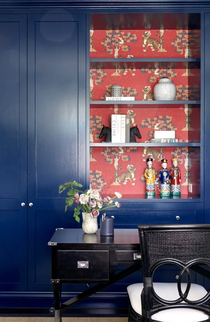 A classic navy style study with open shelving and red tiger wallpaper.