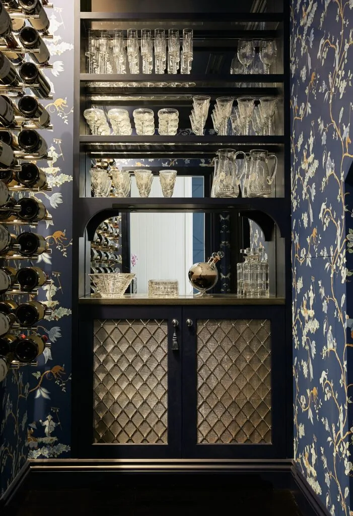 A wine cellar with navy patterned wallpaper and mirrored shelving.