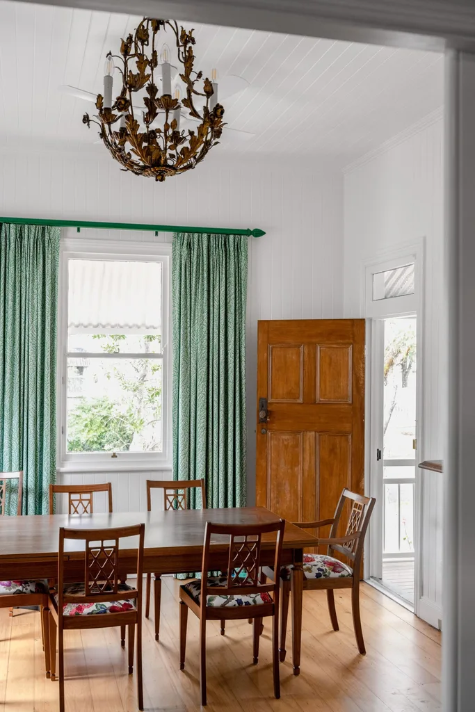 A cottage dining room with a timber table and green curtains.